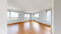 Located on the 21st floor of 1188 Mission Street in San Francisco's SoMa neighborhood, this high-rise residence offers sweeping panoramic views of the city skyline and beyond through its expansive floor-to-ceiling windows. Warm hardwood flooring runs consistently throughout, complementing the clean white walls and creating a bright, cohesive aesthetic across all rooms.

The open living area is generously proportioned, with multiple large windows wrapping around a curved corner column, flooding the space with natural light and framing striking urban vistas. The kitchen is well-appointed with white cabinetry, dark countertops, a full suite of white appliances including a refrigerator and range, and a large window that captures additional city views.

The bedrooms are well-sized, each benefiting from natural light and views of the surrounding cityscape. One bedroom features a built-in closet with shelving. The bathroom is finished in crisp white tile, complete with a soaking tub and shower combination, built-in shelving, and a vanity with a dark countertop. The overall design is clean and contemporary, with a neutral palette that maximizes the sense of openness and highlights the spectacular elevated setting above San Francisco.