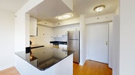 Located at 1450 S Hayes St in Arlington, VA, this one-bedroom, one-bathroom residence offers a thoughtfully arranged layout with hardwood-style flooring throughout. The open-concept living area is a standout feature, anchored by a wall of large windows and a sliding glass door that leads to a private balcony, flooding the space with natural light and offering views of the surrounding Arlington cityscape. The kitchen is well-appointed with dark granite countertops, white cabinetry, stainless steel appliances including a full-size refrigerator, and a peninsula that provides additional prep space and a natural division between the kitchen and living area. A stacked in-unit washer and dryer add everyday convenience. The bedroom is a comfortable, quiet retreat with a window for natural light and direct access to a spacious walk-in closet featuring dual hanging rods and ample shelving. The full bathroom is finished with dark tile flooring, a granite-topped vanity with white cabinetry, a large mirror, and a shower-tub combination. Clean white walls and consistent flooring tie the entire residence together, creating a cohesive and functional living environment.