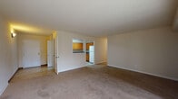 This single-floor unit is designed with a practical, functional layout that makes efficient use of its space. The entryway corridor features a striking design detail — warm recessed wall lighting casting a golden glow between layered white panels, creating a visually dynamic first impression.

The open living area is generously proportioned, finished with neutral-toned carpet and cream-colored walls that contribute to a bright, airy atmosphere. A large sliding glass door fitted with vertical blinds allows natural light to filter in while providing access to the outdoors. The living space connects visually to the kitchen through a pass-through opening, enhancing the sense of openness.

The kitchen is equipped with warm oak cabinetry, dark countertops, and white appliances including a range, dishwasher, and refrigerator. Light tile flooring and ample upper and lower cabinet storage make it a fully functional workspace.

The bedrooms feature soft carpeting and neutral walls, with each room offering closet space — including a walk-in closet in one bedroom. Two bathrooms serve the unit: one includes a tiled tub-shower combination with tile flooring, while the other features a wide vanity with a large mirror and tile flooring, providing convenience and practicality throughout.