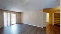 This single-story residence offers a well-organized layout with distinct living, kitchen, bedroom, and bathroom areas. The living room is a spacious, open area finished with dark hardwood-style flooring that extends throughout the main living spaces. Neutral beige walls and a textured popcorn ceiling create a clean, understated backdrop. A sliding glass door fitted with vertical blinds allows natural light to fill the room and provides direct outdoor access. A separate entryway with a white front door transitions smoothly into the main living area.

The kitchen features white cabinetry, including tall upper and lower storage units, light countertops, and a white refrigerator, offering practical functionality. The dark flooring continues here, maintaining visual consistency.

Two bedrooms are finished with plush neutral carpet, white baseboards, and beige walls. Both rooms are brightened by windows fitted with horizontal blinds, with one bedroom benefiting from dual windows for enhanced natural light.

The unit includes two bathrooms. One features a standalone shower with white tile surround, while the other offers a full tub-shower combination. Both bathrooms are equipped with white vanities, single-basin sinks, and wood-style flooring, presenting a consistent, clean aesthetic throughout.