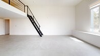 Located at 2735 E 6th St in the heart of East Los Angeles, this modern two-story home offers a thoughtfully designed open-concept layout. The main floor features polished concrete flooring throughout, lending a clean, contemporary aesthetic to the generously sized living, dining, and kitchen area. Bright white walls and multiple windows invite abundant natural light, enhancing the sense of openness. A striking black metal staircase with cable railing serves as a functional architectural focal point, leading to the upper level. The kitchen is well-appointed with warm wood-toned cabinetry, white countertops, a tile backsplash, and stainless steel appliances including a refrigerator, microwave, and range. An in-unit washer is also conveniently integrated into the kitchen area. High ceilings on the main floor add to the airy, loft-like atmosphere. Upstairs, the private bedroom offers a more intimate setting with carpet flooring and an adjoining bathroom complete with a glass-enclosed shower. The overall design balances minimalist modern finishes with practical functionality, making this a well-suited home for those seeking contemporary urban living in Los Angeles.
