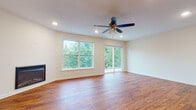 This two-story space is thoughtfully designed with a clean, modern aesthetic that balances functionality and comfort throughout both levels. The main floor opens into a spacious living area anchored by a built-in fireplace and large windows that invite abundant natural light and offer pleasant views of surrounding greenery. Light hardwood-style flooring extends throughout the main level, lending a cohesive, airy feel to the space.

The kitchen is a standout feature, outfitted with rich dark wood cabinetry, light quartz countertops, and a full suite of stainless steel appliances including a range, microwave, dishwasher, and French door refrigerator. A central island with seating provides an ideal space for casual dining or meal preparation. Recessed and pendant lighting illuminate the kitchen effectively. A half bathroom on the main level adds everyday convenience.

A carpeted staircase leads to the upper level, where the bedrooms feature neutral tones, plush carpet flooring, and sliding closet doors offering ample storage. The upper-level bathroom includes a single-sink vanity with dark wood cabinetry, a large mirror, and a walk-in shower, all finished with light luxury vinyl plank flooring. The overall ambiance is bright, clean, and move-in ready.