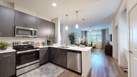 This contemporary single-floor residence showcases a thoughtfully designed open-concept layout that seamlessly connects the kitchen, dining, and living areas. The kitchen is a standout feature, equipped with dark wood cabinetry, crisp white quartz countertops, stainless steel appliances including a range, microwave, dishwasher, and refrigerator, and a peninsula island with bar seating illuminated by modern pendant lighting. Wood-look flooring runs throughout the main living areas, adding warmth and cohesion to the space.

The living room is bright and inviting, benefiting from large windows with blinds and draping curtains that allow generous natural light. A ceiling fan adds comfort, while the open flow from the kitchen creates an ideal setting for entertaining.

Two well-appointed bedrooms feature plush carpeting, oversized windows with outdoor views, ceiling fans, and ample closet space. The primary suite includes a dedicated bathroom with dark wood vanity, white countertop, and a walk-in closet with built-in shelving and hanging rods. A second full bathroom mirrors the same refined aesthetic, complete with a bathtub and large vanity. The overall ambiance is clean, modern, and move-in ready.