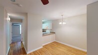 This single-floor, one-bedroom, one-bathroom unit offers a thoughtfully arranged layout that maximizes its compact footprint. The living and dining area features warm hardwood flooring and neutral-toned walls, creating a bright and welcoming atmosphere. A classic chandelier anchors the dining space, adding a touch of elegance. A ceiling fan is also present, contributing to year-round comfort.

The kitchen connects to the dining area via a pass-through opening, promoting an open feel while maintaining a defined cooking space. It is equipped with white cabinetry, a coil-burner electric range, a stainless steel sink, and stone-patterned countertops that continue the cohesive design aesthetic. An overhead exhaust hood provides practical ventilation.

The bedroom is generously proportioned with hardwood flooring and clean white trim. It includes two separate closets with built-in hanging rods, providing ample storage. The flooring transitions to carpet in portions of the bedroom area.

The bathroom is well-finished, featuring a tiled tub-shower combination with large-format wall tiles, a white vanity with stone-patterned countertop, a wide mirror with a multi-bulb light fixture above, and tile flooring. The overall design throughout the unit is clean, consistent, and functional.