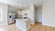 Located at 6408 Providence Farm Ln in Charlotte, NC, this modern three-bedroom, four-bathroom home spans three floors, offering a well-organized layout designed for comfortable living. The ground floor houses an attached garage with an automatic opener, providing convenient and secure parking. Light wood-tone flooring flows consistently throughout the living areas, lending warmth and cohesion to the interior.

The main living floor features an open-concept kitchen and living area. The kitchen is a standout, showcasing two-tone cabinetry — crisp white upper cabinets paired with muted blue-gray lower cabinets — set against a classic white subway tile backsplash. A central island with pendant lighting and a stainless steel sink anchors the space, while stainless steel appliances, including a gas range and a side-by-side refrigerator, complete the chef-friendly setup. The adjoining living area is bright and open, with neutral tones throughout.

The upper floors accommodate three bedrooms, each finished with the same warm hardwood-style flooring and neutral walls, allowing ample natural light through window blinds. The spacious primary bedroom includes its own closet. The four bathrooms are thoughtfully appointed, featuring large-format white tile, a soaking tub, glass-enclosed walk-in showers with chrome hardware, and vanities with stone countertops.