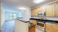 Located at 9030 Lorton Station Blvd, Unit 313 in Lorton, Virginia, this one-bedroom, one-bathroom residence offers a well-organized layout across a single floor. Light-toned hardwood-style flooring runs throughout the main living areas, lending a clean, cohesive aesthetic to the space.

The open-concept kitchen and living room serve as the heart of the unit. The kitchen is outfitted with warm maple cabinetry, dark granite countertops, stainless steel appliances including a range, over-the-range microwave, and refrigerator, and a peninsula that separates the cooking area from the living space. Crown molding adds a polished finish to the living area.

The bedroom is a comfortable, well-proportioned room featuring large windows that invite natural light and offer views of the surrounding greenery. A sliding glass door opens onto a private balcony, extending the living space outdoors with pleasant wooded views.

The bathroom is finished with neutral tile flooring, a warm wood vanity with ample storage, and a full tub-shower combination with tiled surrounds. A hallway connects the rooms efficiently, completing the functional flow of the unit. White panel doors and crisp trim work are consistent throughout, contributing to the space's bright, tidy character.