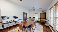 Located at 2900 Old US Highway 63 S in Columbia, Missouri, this single-floor professional workspace is designed to support collaborative work and productivity. The centerpiece of the space is a well-appointed conference room featuring a solid wood rectangular table surrounded by upholstered chairs, ideal for team meetings and group discussions. A large wall-mounted flat-screen display and a generous whiteboard provide ample tools for presentations and brainstorming sessions. A ceiling fan with integrated lighting ensures comfortable airflow throughout the room.

Natural light filters in through multiple windows fitted with wood-trimmed blinds, offering views of the surrounding greenery. The warm, rich hardwood-style flooring runs throughout the space and is complemented by a geometric, multi-colored area rug beneath the conference table, adding a modern touch to the overall aesthetic.

A dedicated computer workstation area is positioned along one wall, equipped with dual desktop monitors and ergonomic seating — well-suited for individual tasks or remote collaboration. Office equipment, including multifunction printers, is conveniently accessible near the whiteboard wall. Dark wood-paneled interior doors add a classic, grounded character to the otherwise clean and contemporary interior. The space is practical, organized, and thoughtfully outfitted for professional use.