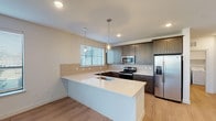 This single-story residence in Spring, Texas offers a thoughtfully designed layout across two bedrooms and two full bathrooms. The open-concept kitchen serves as a central highlight, showcasing dark-toned shaker-style cabinetry paired with crisp white quartz countertops and a matching peninsula with an integrated sink. Stainless steel appliances—including a French door refrigerator, electric range, and built-in microwave—complement the space, while a white subway tile backsplash and neutral tile accent behind the peninsula add visual texture. Pendant lighting and recessed fixtures illuminate the kitchen, which transitions seamlessly onto light wood-look flooring that flows through the main living areas.

The bedrooms feature plush neutral carpeting, blinds for light control, and ceiling fans for added comfort. Both bathrooms are finished with large-format light tile flooring, dark wood vanities topped with granite or stone countertops, and wide mirrors with ample storage. The primary bath features a double-sink vanity and generous cabinetry. Throughout the home, neutral walls, clean white trim, and an abundance of natural light from multiple windows create a bright, modern ambiance.