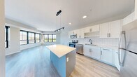 This well-appointed 2-bedroom, 2-bathroom single-floor residence offers a thoughtfully designed open-concept layout that maximizes both functionality and comfort. The kitchen serves as a central highlight, featuring crisp white shaker cabinetry with matte black hardware, a classic white subway tile backsplash, stainless steel appliances including a range, microwave, dishwasher, and refrigerator, and a central island with a light countertop ideal for additional prep space or casual dining. A sleek pendant track lighting fixture adds a modern industrial touch overhead.

The living area flows seamlessly from the kitchen and is bathed in natural light from expansive black-framed windows that frame outdoor views. Light wood-tone flooring runs consistently throughout the space, lending warmth and visual continuity. A clean, neutral color palette of whites and soft grays creates a bright, airy atmosphere throughout.

Both bedrooms are generously sized, each with large windows that invite natural light. The primary bedroom includes a well-organized walk-in closet equipped with built-in wire shelving systems. The bathrooms are finished in a clean, minimalist style, with one featuring a full soaking tub and shower combination. Additional conveniences include a dedicated laundry area and a second closet for added storage. A wide hallway connects the living spaces to the private quarters, completing this practical and modern floor plan.