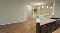 This single-floor space offers a well-designed open-concept layout that seamlessly connects the kitchen and living areas, creating a spacious and functional environment. The kitchen is a standout feature, showcasing rich dark-wood cabinetry paired with a tiled breakfast bar island topped with light granite-style counters. Elegant pendant lights hang above the island, adding a warm and inviting ambiance to the space. The living area extends naturally from the kitchen, bathed in soft, neutral tones on the walls that complement the rich, warm hardwood-style flooring found throughout. The consistent flooring creates a cohesive flow from room to room. A dedicated in-unit laundry area is conveniently accessible from the main living space, providing added practicality. Clean white baseboards and neutral wall colors throughout contribute to a bright, airy feel. The overall design balances comfort and functionality, making it a well-appointed space suited for everyday living.