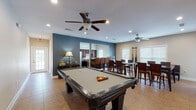 This single-story clubhouse in Atoka, Tennessee, is designed to serve as a versatile community gathering space, offering a well-rounded combination of recreation, dining, and relaxation areas. The layout flows openly between zones, all finished with neutral-toned tile flooring throughout and ceiling fans with integrated lighting in each area.

The centerpiece of the main gathering room is a full-size pool table, positioned beneath recessed lighting and ceiling fans that keep the space comfortable. The room transitions naturally into a dining area furnished with multiple high-top tables and dark wood bar-height chairs, providing generous seating capacity for group events or casual gatherings. Windows along the walls allow natural light to fill the space, and a wall-mounted cue rack keeps billiards equipment neatly organized nearby.

The kitchen is well-appointed with rich, dark wood cabinetry, a stainless steel French-door refrigerator, a dishwasher, microwave, and a built-in bar-style counter with seating. This setup makes the space practical for catering or community events.

A secondary lounge area features a sofa, a wall-mounted television, and a fireplace, accessible through French doors, offering a quieter retreat within the clubhouse. The overall ambiance is welcoming and functional, suited for a wide range of community activities.