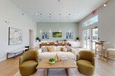 Located at 148 Peabody Rd in Vacaville, CA, this single-floor community space functions as both a leasing office and a resident lounge, offering a thoughtfully designed interior that blends contemporary style with welcoming comfort. The layout is open and airy, anchored by soaring ceilings that amplify the sense of spaciousness throughout.

The entrance foyer greets visitors with a striking sputnik-style chandelier, warm light wood flooring, and glass double doors that flood the space with natural light. A reception desk with guest seating sits just inside, framed by a glass-walled private office nearby. The lounge area transitions seamlessly from the entry, featuring a plush cream sofa, olive-toned accent chairs, and a wood coffee table arranged around a central seating zone. Pendant globe lights with gold accents hang above a counter-height bar area backed by a sage green accent wall adorned with curated artwork and a wall-mounted television.

Floor-to-ceiling windows and glass doors along one side of the space provide direct views of an outdoor pool area, bathing the interior in sunlight. High clerestory windows further enhance the bright, open ambiance. Light wood flooring runs throughout, tying the zones together cohesively. The overall design aesthetic is modern and polished, with warm gold fixtures and carefully selected furnishings creating an inviting and functional community environment.