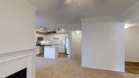 This two-floor Arlington residence offers a well-designed open-concept layout that seamlessly connects the living and kitchen areas. The kitchen is a standout feature, outfitted with crisp white cabinetry, stainless steel appliances including a refrigerator, microwave, and range, and a central island that provides additional prep and casual dining space. Track lighting overhead ensures the kitchen is well-illuminated at all times. The adjacent living area is finished with plush neutral carpeting, creating a warm and comfortable atmosphere. Crown molding and clean white walls contribute to a polished, classic aesthetic throughout the main level. Vaulted ceilings add a sense of openness and grandeur, making the shared living spaces feel expansive and airy. A ceiling fan in the living area enhances comfort year-round. The neutral color palette and consistent finishes create a cohesive, move-in-ready environment. With two floors, the layout offers a natural separation between living and private spaces, providing both functionality and flexibility. This Arlington home combines practical design with refined details for comfortable everyday living.