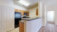 This single-floor residence offers a practical and well-organized layout designed for comfortable everyday living. The kitchen is equipped with warm honey-toned wood cabinetry, dark laminate countertops, and a full suite of black appliances including a refrigerator, electric range, and over-the-range microwave. A peninsula counter extends into the living area, providing additional prep space and a casual dining option while maintaining an open connection between the kitchen and the rest of the unit. Wood-look flooring runs throughout the main living areas, lending a clean and cohesive aesthetic. The bedrooms feature plush carpeting and ceiling fans, with natural light provided by windows overlooking the exterior. Walk-in closet space offers generous storage and organizational flexibility. The bathrooms are appointed with wood-toned vanity cabinetry, dark countertops, and tub-shower combinations, all set on wood-look flooring for easy maintenance. A dedicated in-unit laundry room includes a full-size washer and dryer, a utility sink, and overhead shelving, adding significant convenience. The overall design is neutral and functional, with beige walls, white trim, and consistent finishes throughout that create a cohesive and move-in-ready environment.