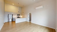 Located at 11501 Clear Creek Rd NW in Silverdale, WA, this thoughtfully designed 2-bedroom, 2-bathroom residence offers a clean, contemporary aesthetic across a well-planned single-floor layout. The open-concept living, dining, and kitchen area serves as the heart of the home, highlighted by soaring ceilings that lend a striking sense of volume and airiness. The kitchen features sleek gray cabinetry, stainless steel appliances including a refrigerator and microwave, a white peninsula with pendant lighting overhead, and a subway tile backsplash. Light wood-tone flooring flows throughout the main living areas, complementing the bright, neutral color palette. A wall-mounted mini-split system provides efficient climate control in both the living area and primary bedroom. The primary bedroom is generously sized with direct access to a private balcony overlooking the surrounding neighborhood, a ceiling fan, and a connected bathroom. The secondary bedroom offers plush carpeting and a large window with neighborhood views. Three closets provide ample storage, including a walk-in closet with wire shelving. The bathrooms are finished with wood-look flooring and marble-style tile surrounds. A dedicated laundry area and entrance complete this well-appointed residence.