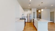 This well-designed 2-bedroom, 2-bathroom residence offers a clean, modern aesthetic with light wood-style flooring and crisp white walls throughout. The open-concept kitchen and living area serves as the heart of the home, featuring a large central island with a built-in sink and white quartz countertops, white shaker-style cabinetry, a white subway tile backsplash, and stainless steel appliances including a refrigerator and range. Stylish globe pendant lights hang above the island, adding a contemporary touch. The adjacent living area is bright and airy, with two windows that invite natural light and a ceiling fan overhead. Both bedrooms continue the light, neutral palette with the same wood-style flooring, ceiling fans, and windows offering exterior views — creating comfortable, well-lit retreats. Two closets provide ample storage. The bathrooms are finished with white shaker vanities, quartz countertops, brushed nickel fixtures, large mirrors, and combination tub-shower units with tiled surrounds. The overall ambiance is clean, contemporary, and move-in ready, with consistent finishes that lend a cohesive, polished feel throughout the entire space.