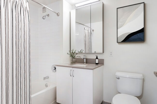 Renovated Package I bath with grey quartz countertop, white cabinetry, and hard-surface flooring (Representative Imagery) - Avalon Riverview