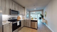 This thoughtfully designed single-floor residence showcases a contemporary aesthetic with a seamless open-concept layout. The kitchen is a standout feature, offering an abundance of wood-toned cabinetry extending to the ceiling, a white subway tile backsplash, light quartz countertops, and a full suite of stainless steel appliances including a refrigerator, electric range, over-the-range microwave, and dishwasher. Pendant lighting adds warmth above the kitchen peninsula, which opens directly into the living and dining areas. The living room is bright and welcoming, featuring large windows dressed with blinds and sheer curtains that flood the space with natural light. Light wood-style flooring runs throughout the main living areas, providing a clean, cohesive look. The bedrooms are carpeted for comfort and each feature generous windows, ceiling fans, and ample space. The primary bedroom connects to a well-appointed en-suite bathroom complete with a soaking tub, tiled surround, and a double-sink vanity with wood-toned cabinetry. A secondary bathroom mirrors this refined style with a tub-shower combination and clean white tile. A dedicated in-unit laundry closet adds everyday convenience, completing this well-equipped and stylishly finished residence.