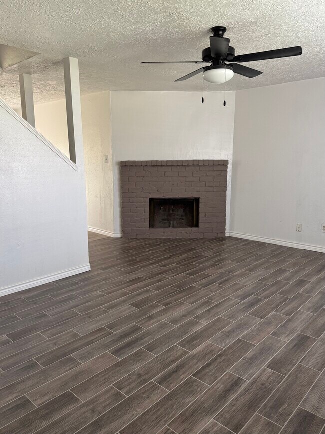 Luminoso salón con elegantes suelos de imitación madera y una acogedora pared decorativa con chimenea. - 10038 Spring Place Dr