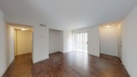 This single-story space is defined by rich, dark hardwood flooring that runs consistently throughout the main living areas and bedrooms, creating a warm and cohesive aesthetic. The open layout connects a spacious living area to an adjoining room, offering flexible use of the floor plan. A sliding glass door in the living area allows natural light to filter in and provides direct access to the outdoors, while additional windows in the secondary rooms contribute to a bright, airy atmosphere.

The kitchen is designed in a galley configuration, lined with white cabinetry, granite-style countertops, and a full suite of stainless steel appliances, including a refrigerator, range, and over-the-range microwave. Tile backsplash adds a clean, finished look to the space.

The bathroom continues the updated aesthetic with white cabinetry, a granite countertop, an undermount sink, and tile flooring. Closet spaces are integrated into the bedroom areas, offering practical built-in storage. Throughout the unit, clean white walls and smooth ceilings complement the neutral palette, resulting in a move-in-ready space with a modern, understated character.