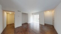 This single-story space is defined by rich, dark hardwood flooring that runs consistently throughout the main living areas and bedrooms, creating a warm and cohesive aesthetic. The open layout connects a spacious living area to an adjoining room, offering flexible use of the floor plan. A sliding glass door in the living area allows natural light to filter in and provides direct access to the outdoors, while additional windows in the secondary rooms contribute to a bright, airy atmosphere.

The kitchen is designed in a galley configuration, lined with white cabinetry, granite-style countertops, and a full suite of stainless steel appliances, including a refrigerator, range, and over-the-range microwave. Tile backsplash adds a clean, finished look to the space.

The bathroom continues the updated aesthetic with white cabinetry, a granite countertop, an undermount sink, and tile flooring. Closet spaces are integrated into the bedroom areas, offering practical built-in storage. Throughout the unit, clean white walls and smooth ceilings complement the neutral palette, resulting in a move-in-ready space with a modern, understated character.