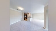 Located at 100 Crossroads Loop in Yorktown, Virginia, this single-story residence offers a well-organized, open-concept floor plan designed for comfortable everyday living. The main living area is expansive and carpeted, with neutral-toned walls and clean crown molding that contribute to a bright, cohesive aesthetic. A dedicated entryway with hard-surface flooring provides a functional transition into the living space.

The kitchen is efficiently designed with rich dark-wood cabinetry, stainless steel appliances including a range, microwave, and refrigerator, and a peninsula with a granite-style countertop that connects seamlessly to the living area. Hard-surface flooring runs throughout the kitchen, complementing the warm cabinetry tones.

The bedrooms are carpeted and receive natural light through windows with exterior views of the surrounding neighborhood. Each room offers generous wall space suitable for a variety of furniture arrangements. The bathroom features tile flooring, a dark-wood vanity with a white countertop, and a full tub-shower combination with white tile surround. An adjacent walk-in closet adds practical storage. The overall ambiance throughout the unit is clean, neutral, and move-in ready.