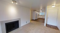 This single-floor, 2-bedroom, 2-bathroom residence offers a practical and comfortable layout designed to maximize everyday living. The living room serves as a welcoming central gathering space, featuring a tile-surround fireplace that adds warmth and character to the room. Soft carpet flooring extends throughout the living area, creating a cozy and inviting atmosphere.

The living space opens directly into the kitchen, which is outfitted with white cabinetry, white appliances including a refrigerator and range, and a sink positioned beneath a window that brings in natural light from the surrounding greenery outside. The kitchen features durable hardwood-style flooring, providing a clean contrast to the carpeted living area. A ceiling fan in the kitchen adds both function and airflow to the space.

The neutral color palette of cream and white tones throughout the home creates a bright, clean aesthetic that complements the natural light filtering in. The open connection between the living and kitchen areas fosters an easy flow for daily routines and entertaining. With two bedrooms and two bathrooms, this well-appointed residence offers ample space for comfortable living in a functional, single-level floor plan.