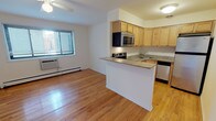 This single-floor unit offers a well-organized, open-concept layout that seamlessly connects the living area to the kitchen. Warm hardwood flooring extends throughout the main living space, adding a welcoming brightness complemented by white walls and ceiling fans that provide both light and air circulation. A large window in the living area allows natural light to fill the room, while a wall-mounted HVAC unit and baseboard heater ensure year-round comfort.

The kitchen is defined by a peninsula counter with a granite-style surface that separates it from the living area, creating a natural divide without sacrificing openness. Light maple cabinetry lines the walls, offering generous storage, while the full suite of stainless steel appliances — including a refrigerator, electric range, built-in microwave, and dishwasher — provides modern functionality. A corner sink with additional counter space completes this efficient, well-appointed kitchen.

The bathroom is clean and classically designed, featuring a full soaking tub with an overhead shower, white square-tile surround, and chrome fixtures. The overall ambiance of the unit is bright, tidy, and practical, making excellent use of its compact footprint while maintaining a comfortable and livable atmosphere throughout.