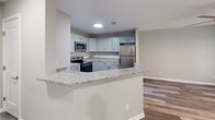 Located at 1523 Roswell Rd in Marietta, GA, this one-bedroom, one-bathroom unit offers a well-designed, efficient layout across a single floor. The kitchen is a standout feature, showcasing gray shaker-style cabinetry, granite countertops, a subway tile backsplash, and a full suite of stainless steel appliances including a refrigerator, electric range, and built-in microwave. A peninsula with a granite overhang provides additional counter space and opens to the living area, creating an open, connected feel. The kitchen and living areas are finished with durable hardwood-style plank flooring in a light gray tone, lending a clean, contemporary aesthetic throughout. The bedroom is a comfortable, well-proportioned retreat featuring plush wall-to-wall carpeting, a ceiling fan with light fixture, and a window that brings in natural light. A dedicated walk-in closet offers generous storage. The bathroom continues the cohesive design language of the home, with a gray vanity topped with granite, a large mirror with vanity lighting, hardwood-style flooring, and a tiled tub/shower combination. Neutral wall tones and consistent finishes throughout create a polished, move-in-ready living space.