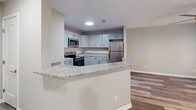 Located at 1523 Roswell Rd in Marietta, GA, this one-bedroom, one-bathroom unit offers a well-designed, efficient layout across a single floor. The kitchen is a standout feature, showcasing gray shaker-style cabinetry, granite countertops, a subway tile backsplash, and a full suite of stainless steel appliances including a refrigerator, electric range, and built-in microwave. A peninsula with a granite overhang provides additional counter space and opens to the living area, creating an open, connected feel. The kitchen and living areas are finished with durable hardwood-style plank flooring in a light gray tone, lending a clean, contemporary aesthetic throughout. The bedroom is a comfortable, well-proportioned retreat featuring plush wall-to-wall carpeting, a ceiling fan with light fixture, and a window that brings in natural light. A dedicated walk-in closet offers generous storage. The bathroom continues the cohesive design language of the home, with a gray vanity topped with granite, a large mirror with vanity lighting, hardwood-style flooring, and a tiled tub/shower combination. Neutral wall tones and consistent finishes throughout create a polished, move-in-ready living space.