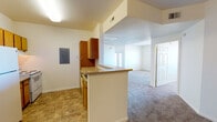 This single-floor residence offers a practical and well-organized layout designed for comfortable everyday living. The kitchen is a functional galley-style space equipped with warm wood-toned cabinetry, white appliances including a refrigerator and electric range, a tile-pattern floor, and a peninsula counter that opens toward the living area — creating a natural flow between cooking and entertaining spaces. An electrical panel is conveniently located within the kitchen area.

The open living room extends generously from the kitchen, featuring plush carpeting and a raised architectural soffit that adds visual definition to the space. Multiple doorways connect the living area to the bedrooms, providing easy circulation throughout the unit.

The bedrooms are bright and inviting, each finished with soft carpeting and windows that allow natural light to fill the rooms and offer views of the surrounding neighborhood. The rooms are well-proportioned, providing ample space for furnishings.

The bathroom is cleanly appointed with a tiled tub-and-shower combination, a wood-cabinet vanity with a single sink, a large mirror with overhead lighting, and matching tile flooring. Accessibility grab bars are installed at the tub and toilet areas, adding a practical and inclusive touch to the design. Overall, the space maintains a clean, neutral palette throughout.