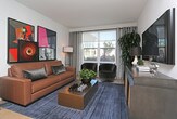 Located at 100 E Grand Ave in South San Francisco, this single-floor residence offers a well-organized layout with a contemporary design aesthetic throughout. The open-concept floor plan connects the living and kitchen areas seamlessly, creating a cohesive and functional living environment.

The living area features large windows with floor-to-ceiling drapes, allowing ample natural light to fill the space. Neutral walls and light flooring complement the modern furnishings, while the room comfortably accommodates a full seating arrangement.

The kitchen is outfitted with light wood cabinetry, gray subway tile backsplash, white countertops, and stainless steel appliances, including a gas range, built-in microwave, and full-size refrigerator. Light hardwood flooring adds warmth to the cooking space.

The bedrooms feature plush carpeting, large windows with outdoor views, and soft neutral tones. One bedroom includes a full-wall mirror that enhances the sense of space, while both rooms offer comfortable proportions and natural light.

The bathroom is finished with wood-toned cabinetry, a white countertop, a soaking tub with shower, and gray accent walls. A hallway connects the rooms efficiently, completing this well-appointed single-level residence.