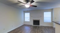 Located at 131 Woodchase Park Dr in Clinton, Mississippi, this single-story home offers a comfortable and functional layout designed for easy living. The living area serves as the heart of the home, showcasing rich, dark hardwood-style flooring that extends throughout the space, lending warmth and a polished aesthetic. A classic tiled fireplace with a clean white mantel serves as a natural focal point, providing both charm and a cozy atmosphere. Natural light filters in through multiple windows fitted with blinds, brightening the room while allowing for privacy control. A ceiling fan with an integrated light fixture is centrally mounted, ensuring year-round comfort and efficient air circulation. The walls are finished in a neutral tone, offering a versatile backdrop that complements a variety of décor styles. The overall ambiance of the space is welcoming and well-maintained, reflecting a straightforward, move-in-ready character. The single-floor layout ensures seamless accessibility throughout, making it a practical and inviting place to call home in the heart of Clinton, MS.