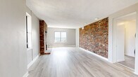 Located at 42 Wyoming St in Pittsburgh's Mt. Washington neighborhood, this well-appointed 2-bedroom, 2-bathroom unit offers a thoughtful layout across a single floor. The open living room serves as the heart of the home, anchored by a striking floor-to-ceiling brick fireplace and shiplap accent wall. Light hardwood-style flooring runs throughout, and multiple windows frame sweeping panoramic views of the Pittsburgh skyline and rivers below.

The updated kitchen features soft gray shaker cabinets, crisp white countertops, stainless steel appliances, and coffered ceiling detailing — combining style with functionality. Both bedrooms are carpeted and bathed in natural light; the primary bedroom boasts dual windows with expansive city views, while the secondary bedroom offers a cozy, quiet retreat.

The two bathrooms differ in style: one is a modern, fully tiled bath with a glass-enclosed walk-in shower, mosaic tile flooring, and a wood-accented vanity, while the second is a classic full bath with a tub-shower combo and glass block windows. An in-unit laundry area houses a stacked Samsung washer and dryer. The unit also includes access to a shared balcony overlooking the neighborhood rooftops and Pittsburgh's vibrant cityscape.