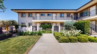 Located at 256–268 Erbes Road in Thousand Oaks, California, this residential community presents a polished exterior defined by warm stucco facades, dark-trimmed balconies, and ornamental iron gate entries. Manicured hedges, flowering plants including agapanthus and roses, and neatly edged lawns frame the front walkways, creating an inviting first impression that reflects thoughtful, well-maintained landscaping throughout.

The heart of the community is a beautifully designed outdoor courtyard that serves as a central gathering space. A substantial pergola, supported by stacked-stone columns and strung with overhead lighting, provides shaded seating areas furnished with comfortable lounge furniture arranged around fire pit-style tables. Blooming crape myrtle trees in vibrant pink add seasonal color, while raised planters and ornamental shrubs contribute layers of greenery. A decorative water fountain anchors one corner of the courtyard, enhancing the tranquil ambiance.

The building architecture blends Mediterranean and California contemporary influences, with covered walkways, stone-accented pergola entryways, and upper-level balconies that overlook the landscaped grounds. The layout of the community, as revealed in the 3D scan, reflects a thoughtfully arranged complex with interconnected outdoor spaces designed to encourage community interaction while maintaining a serene, resort-like atmosphere under the abundant Southern California sunshine.