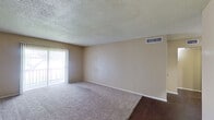 This single-floor residence offers a functional and straightforward layout designed to maximize everyday comfort. The living room serves as the central gathering space, featuring plush wall-to-wall carpeting, neutral beige walls, and a textured ceiling. A full-length sliding glass door with vertical blinds floods the room with natural light and provides access to an outdoor balcony or patio area, while dark hardwood-style flooring accents the entryway transition.

The galley-style kitchen is efficiently arranged with dark wood cabinetry lining both sides, offering generous storage above and below. White appliances include a coil-top electric range, refrigerator, and dishwasher, complemented by a double stainless steel sink and laminate countertops beneath bright overhead lighting.

The bedrooms are carpeted and finished with the same warm neutral tones found throughout the unit. One bedroom features a ceiling fan with light fixture and a window with blinds for natural light, while another includes a spacious walk-in closet with built-in shelving and rod storage.

The bathroom is clean and functional, equipped with a full-sized tub and shower combination with tiled surround, dark hardwood-style flooring, and a vanity with granite-style countertop. Throughout the unit, a consistent neutral palette and practical finishes create a cohesive and move-in-ready living environment.
