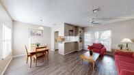Located at 5622 Evers Rd in San Antonio, TX, this single-floor unit offers a well-organized, open-concept layout that connects the living, dining, and kitchen areas seamlessly. The living room features durable hardwood-style flooring, a ceiling fan with light fixture, built-in shelving, and a glass-paneled door that allows generous natural light to filter in while providing outdoor access. Adjacent to the living area, the dining space accommodates a four-person table beneath a pendant light fixture, with a nearby window adding additional brightness. The galley-style kitchen is outfitted with white cabinetry, light countertops, a double-basin sink, and a coil-burner electric range, with a pass-through opening that maintains visual connectivity to the dining area. The unit includes two bedrooms, each carpeted and equipped with ceiling fans, windows with blinds, and ample closet space — one bedroom features a spacious walk-in closet with shelving and hanging rods. The bathroom presents a white vanity with a framed mirror, louvered cabinet, and hardwood-style flooring consistent with the rest of the unit. Textured ceilings and neutral warm-toned walls are carried throughout, creating a cohesive and functional living environment.