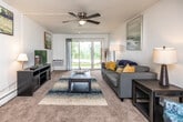 This single-floor residence offers a thoughtfully organized layout with two bedrooms, a living area, kitchen, dining space, and a full bathroom. The living room serves as the central gathering space, featuring wall-to-wall carpeting, a ceiling fan, and a textured ceiling. Large sliding glass doors along one wall flood the room with natural light and provide direct views of the surrounding greenery, creating an open, airy atmosphere. The adjoining dining area flows seamlessly into the kitchen, which is equipped with warm oak cabinetry, granite-style countertops, a double-basin sink, and black appliances including a refrigerator and range. Tile flooring runs through the kitchen and dining zone, providing a practical transition from the carpeted living spaces. Both bedrooms are comfortably proportioned, each featuring soft carpet, neutral walls, and sliding-door closets offering ample storage. The primary bedroom benefits from a large window that brings in generous natural light and outdoor views. The bathroom is cleanly finished with a white vanity, tub-shower combination, and tile flooring, completing this well-appointed, move-in-ready residence.