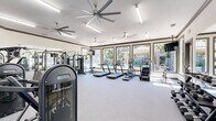 Located at 40 Park City Ct in Sacramento, California, this fitness center offers a well-appointed, single-floor exercise space designed to support a full range of workout routines. The room is finished with durable grey carpeting and features clean white walls accented by warm grey trim, creating a bright and motivating environment. Large ceiling fans provide consistent airflow throughout the space, complementing the flush linear lighting overhead.

The facility is comprehensively equipped with a diverse selection of fitness machines, including dual treadmills, an elliptical, a stationary bike, and a cable crossover machine. Dedicated strength training stations feature adjustable weight machines, a multi-purpose power rack with a flat bench, and a full rack of dumbbells for free weight exercises. A stability ball and wall-mounted mirrors further support varied training needs.

Natural light fills the space through a bank of large windows that frame a picturesque view of a resort-style pool area surrounded by flowering trees — an inviting backdrop during cardio sessions. A wall-mounted television adds an entertainment option for users. Multiple glass-panel entry doors provide convenient access points from both the interior and exterior, enhancing the open, accessible feel of this well-rounded fitness facility.