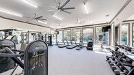 Located at 40 Park City Ct in Sacramento, California, this fitness center offers a well-appointed, single-floor exercise space designed to support a full range of workout routines. The room is finished with durable grey carpeting and features clean white walls accented by warm grey trim, creating a bright and motivating environment. Large ceiling fans provide consistent airflow throughout the space, complementing the flush linear lighting overhead.

The facility is comprehensively equipped with a diverse selection of fitness machines, including dual treadmills, an elliptical, a stationary bike, and a cable crossover machine. Dedicated strength training stations feature adjustable weight machines, a multi-purpose power rack with a flat bench, and a full rack of dumbbells for free weight exercises. A stability ball and wall-mounted mirrors further support varied training needs.

Natural light fills the space through a bank of large windows that frame a picturesque view of a resort-style pool area surrounded by flowering trees — an inviting backdrop during cardio sessions. A wall-mounted television adds an entertainment option for users. Multiple glass-panel entry doors provide convenient access points from both the interior and exterior, enhancing the open, accessible feel of this well-rounded fitness facility.