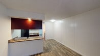 This single-floor unit offers a cohesive and practical layout highlighted by wood-look flooring that runs seamlessly throughout every room. The entryway welcomes you with a wide window that frames natural light, setting a bright and airy tone from the moment you step inside.

The open living area features a distinctive vertical panel accent wall, adding a subtle textural detail to the clean, neutral interior. A textured ceiling is present throughout the unit, lending a classic residential character to the space.

The galley-style kitchen is efficiently designed with rich, dark cabinetry, granite-style countertops, and black appliances including a gas range and full-size refrigerator. A stainless steel sink and under-cabinet range hood complete the functional setup, while a breakfast bar provides a convenient pass-through connection to the living area.

The bedroom is a generously sized room bathed in natural light from a wide exterior-facing window, offering views of the surrounding neighborhood. The neutral walls and consistent flooring create a calm and versatile environment.

The bathroom includes built-in open shelving that provides ample storage, along with a vanity featuring matching granite-style countertops. Direct access to the bedroom enhances the flow of the layout. Overall, the space presents a clean, move-in-ready interior with consistent finishes throughout.