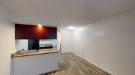 This single-floor unit offers a cohesive and practical layout highlighted by wood-look flooring that runs seamlessly throughout every room. The entryway welcomes you with a wide window that frames natural light, setting a bright and airy tone from the moment you step inside.

The open living area features a distinctive vertical panel accent wall, adding a subtle textural detail to the clean, neutral interior. A textured ceiling is present throughout the unit, lending a classic residential character to the space.

The galley-style kitchen is efficiently designed with rich, dark cabinetry, granite-style countertops, and black appliances including a gas range and full-size refrigerator. A stainless steel sink and under-cabinet range hood complete the functional setup, while a breakfast bar provides a convenient pass-through connection to the living area.

The bedroom is a generously sized room bathed in natural light from a wide exterior-facing window, offering views of the surrounding neighborhood. The neutral walls and consistent flooring create a calm and versatile environment.

The bathroom includes built-in open shelving that provides ample storage, along with a vanity featuring matching granite-style countertops. Direct access to the bedroom enhances the flow of the layout. Overall, the space presents a clean, move-in-ready interior with consistent finishes throughout.