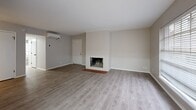 This single-floor residence offers a well-designed layout that balances comfort and modern updates throughout. The expansive living area is a standout feature, showcasing light gray hardwood-style flooring, a white brick fireplace with a classic terracotta tile hearth, and multiple windows fitted with horizontal blinds that allow abundant natural light to fill the space. A wall-mounted mini-split unit provides climate control, and an open flow connects the living area to an adjacent room with its own large window, also finished with the same light hardwood-style flooring.

The kitchen has been thoughtfully updated with two-tone cabinetry — white upper shaker-style cabinets and gray lower cabinets — paired with quartz countertops and a white subway tile backsplash. Black appliances, including a range, microwave, and refrigerator, add a bold contrast, while light wood-look flooring and a stainless steel sink complete the functional space.

The bedrooms feature soft, neutral carpet and windows that bring in natural light, creating comfortable and quiet retreats. The bathroom is finished with gray cabinetry, a white quartz vanity top, matte black fixtures and hardware, a tiled walk-in shower, and access to a closet area — delivering a clean, contemporary aesthetic throughout.