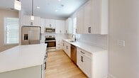 Located at 203 29th Ave NE in Hickory, NC, this two-story home offers a clean, modern aesthetic with thoughtfully designed living spaces spread across two floors. The main level features warm hardwood flooring throughout the open living room and kitchen area, bathed in natural light from multiple windows dressed with white blinds. The kitchen is a standout, showcasing crisp white shaker cabinets with matte black hardware, white quartz countertops, a classic subway tile backsplash, a center island with pendant lighting, and a full suite of stainless steel appliances. Recessed lighting adds a polished finish to the space. The upper floor hosts all three bedrooms, each carpeted in neutral tones and filled with natural light. The spacious primary bedroom features dual windows and a ceiling fan, creating a bright and comfortable retreat. The additional bedrooms are well-sized with clean white walls and white panel doors. A dedicated closet with wire shelving provides ample storage. The full bathroom is bright and functional, featuring white cabinetry, quartz countertops, an undermount sink, a large mirror, and a shower-tub combination. Two hallways connect the layout efficiently across both levels, completing this move-in-ready home.