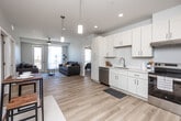 Located at 565 Market St in West Des Moines, Iowa, this well-appointed 2-bedroom, 2-bathroom unit offers a thoughtfully designed open-concept layout with modern finishes throughout. Light-toned hardwood flooring flows seamlessly through the combined kitchen and living area, creating a bright and cohesive main living space. The kitchen is equipped with white shaker cabinetry, stainless steel appliances including a dishwasher and refrigerator, a clean white countertop, and pendant lighting that adds a contemporary touch. The living room benefits from abundant natural light and direct access to a private balcony through a glass-panel door, offering outdoor views of the surrounding area. Both bedrooms feature plush carpeting, large windows for natural light, and ceiling fans. Each bedroom is served by its own walk-in closet outfitted with wire shelving systems for organized storage. The primary bathroom is particularly spacious, showcasing large-format marble-look tile flooring, a dual-sink vanity with white cabinetry, and a soaking tub with shower. The overall ambiance is clean, neutral, and modern, making this a comfortable and functional residence in the heart of West Des Moines.