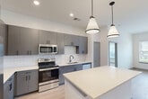 Located on Populus Loop in Chattanooga, TN, this well-appointed 2-bedroom, 2-bathroom residence offers a thoughtfully designed single-level layout. The open-concept kitchen and living area serves as the heart of the home, showcasing sleek gray cabinetry, a geometric white tile backsplash, stainless steel appliances, and a central island with light quartz countertops illuminated by stylish pendant lighting. Light wood-look flooring runs throughout the main living areas, lending warmth and continuity to the modern aesthetic. The living area features a built-in desk nook and recessed lighting, creating a functional yet clean space. Both bedrooms are carpeted for comfort, with large windows that invite natural light and offer views of the surrounding community. The primary bedroom includes access to a walk-in closet with multi-tier wire shelving, providing ample organized storage. A total of four closets throughout the residence ensures generous storage options. The bathrooms feature gray vanities with white countertops, black hardware accents, and wood-look flooring that complements the overall design palette. A dedicated laundry area adds everyday convenience. Neutral tones and contemporary finishes are carried consistently throughout, creating a cohesive and move-in-ready living environment.