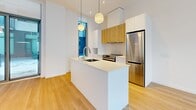 Located at 2812 Rue Ontario E in Montréal's vibrant Hochelaga-Maisonneuve neighbourhood, this modern one-bedroom, one-bathroom unit offers a thoughtfully designed living space with a clean, contemporary aesthetic. Light hardwood flooring flows seamlessly throughout, complementing the bright white walls and creating a warm, cohesive atmosphere.

The open-concept kitchen is a standout feature, anchored by a sleek white waterfall island with an integrated sink. A mix of white and natural wood-toned cabinetry lines the walls, paired with a subway tile backsplash, stainless steel appliances including a full-size refrigerator and range, and stylish globe pendant lights that hang above the island, adding a modern touch to the space.

The bedroom is a calm, well-proportioned retreat, featuring tall floor-to-ceiling windows that invite abundant natural light and provide views to the exterior. A sliding closet door and a baseboard heating unit complete the room's practical layout.

The bathroom is finished with warm beige floor tiles and large-format wall tiles surrounding the soaker tub and shower combo. A wood-fronted vanity with a white countertop and an integrated sink adds a refined, cohesive look. The overall design of this unit prioritizes clean lines, natural materials, and functional living — ideal for those seeking a modern urban residence in Montréal.