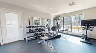 Located at 12801 Indian School Rd NE in Albuquerque, New Mexico, this fitness center offers a comprehensive workout facility spread across a single floor. The space is divided into two distinct functional zones designed to accommodate a full range of exercise routines.

The cardio area is bathed in natural light from large, multi-pane windows that line the walls, offering views of the surrounding exterior. This section houses modern cardio equipment including a treadmill, elliptical trainer, and rowing machine, all positioned to take advantage of the bright, open atmosphere. Recessed lighting in the ceiling supplements natural light throughout the day.

The strength training area features Hoist cable machines, a multi-position adjustable bench, and a well-stocked dumbbell rack with a full range of free weights. A large wall mirror enhances the sense of space while allowing users to monitor their form. Medicine balls and TRX-style suspension trainers are also available for functional fitness training.

Throughout the facility, durable rubber flooring provides safety and stability underfoot, while white walls and a neutral color palette create a clean, focused environment. Structural columns define the open floor plan without interrupting the flow between zones. The space is accessible via an exterior door and is well-ventilated with ceiling vents, making it a functional and inviting fitness facility.