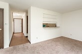This two-floor residential space offers a practical and functional layout designed for comfortable everyday living. The main living area is finished with neutral-toned wall-to-wall carpeting and features a textured ceiling. A standout architectural detail is the pass-through opening between the living room and kitchen, complete with built-in shelving above, which adds an open, connected feel to the shared living space.

The kitchen is efficiently laid out in a galley style, featuring warm honey-toned wood cabinetry, light laminate countertops, wood-look flooring, and includes appliances such as a coil-top electric range and a dishwasher. A dedicated laundry area accommodates a full-size washer and dryer, with additional overhead cabinetry for storage.

The bedrooms are carpeted and offer ample space, with clean white walls and textured ceilings. One bedroom benefits from a window that brings in natural light and an outdoor view, while another area features a large sliding glass door that opens to a view of a landscaped exterior. The bathroom includes a full tub and shower combination, a wood-cabinet vanity with a white countertop, and wood-look flooring. A half bath with hardwood-style flooring is also present. Throughout the space, dark wood interior doors provide consistent design continuity.