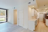 This thoughtfully renovated single-floor unit showcases a clean, contemporary design centered around a bright white-and-gold color palette that carries consistently throughout every room. Light-toned large-format tile flooring runs across the open living and dining areas, reflecting natural light and enhancing the sense of openness. A floor-to-ceiling sliding glass door in the living area frames views of lush greenery outside, flooding the space with abundant natural light.

The galley-style kitchen is a standout feature, equipped with white shaker cabinetry accented by brushed gold hardware, quartz countertops, a subway tile backsplash, a gold-tone undermount sink with a designer faucet, and a full suite of stainless steel appliances. An adjacent wet bar or prep area extends the kitchen's functionality with additional counter space and cabinetry.

The bedroom is a serene, sunlit retreat with generous proportions and the same light-toned flooring, providing a calm and neutral canvas. The bathroom is elegantly appointed with a white vanity featuring gold fixtures, a round gold-framed mirror, and a walk-in glass-enclosed shower clad in full-height marble-look porcelain tile with a contrasting penny-tile mosaic floor — a refined finishing touch that elevates the overall design of this meticulously updated space.
